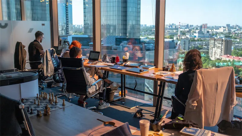 Bureau avec des personnes travaillant à des bureaux, vue sur la ville à travers les fenêtres.