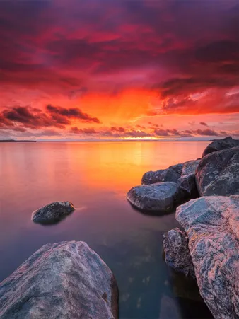 Coucher de soleil sur l'eau, avec des rochers au premier plan, créant une scène paisible et colorée.